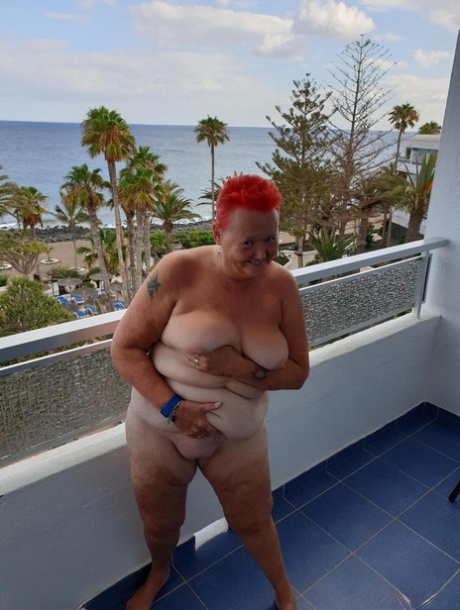 Exposed and slickly donning short red hair, the overweight vampiricist is sitting naked on an open balcony with no back support.