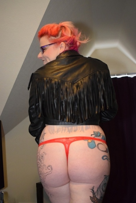 A tattooed redhead removes her leather clothes to model in risqué lingerie.