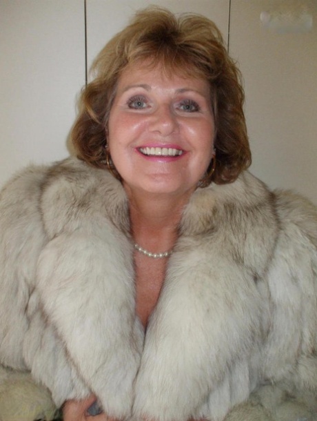 Busty Bliss, an older woman, licks her lips and then wears a fur coat that showcases her breasts.