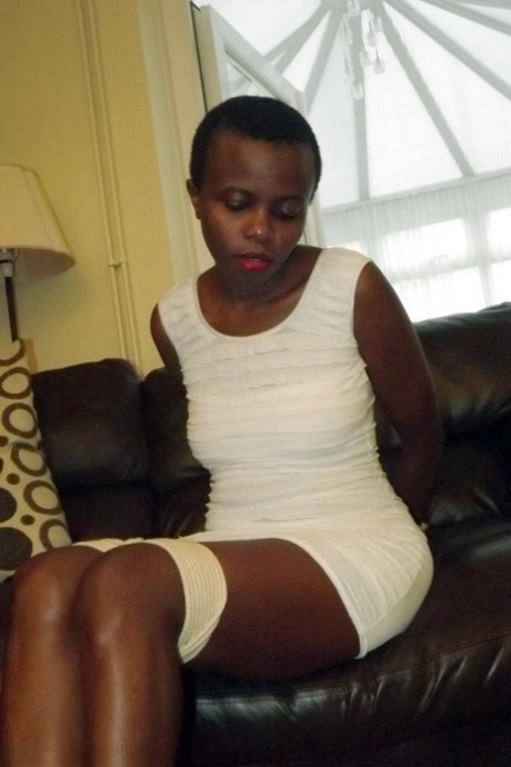 Черная женщина остается связанной и с кляпом во рту в белом платье на кожаном диване