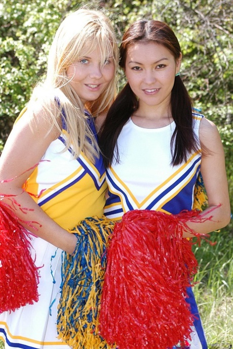 Cheerleaders engage in interracial lesbian sex near scrubby bushes.