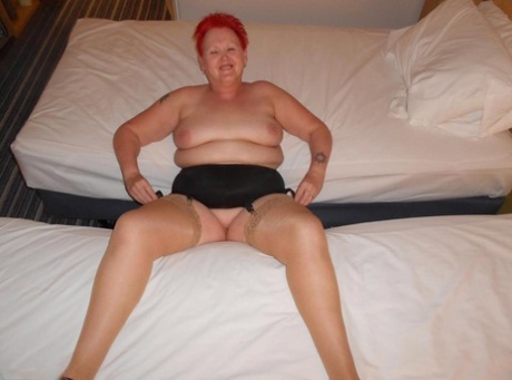 On a bed, naked on the floor, Vagasmic Exposed, an overweight redhead who is dressed in jeans and high heels, poses.