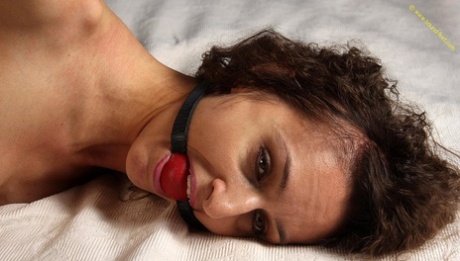 The girl is left lying on a bed with her top down, while being ballgged and hogtied.