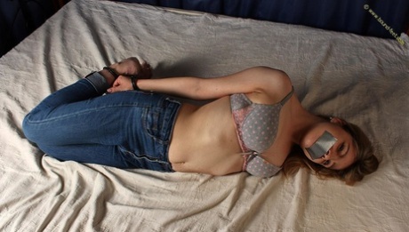 With duct tape covering her mouth, the white girl is tied up on an open bed.