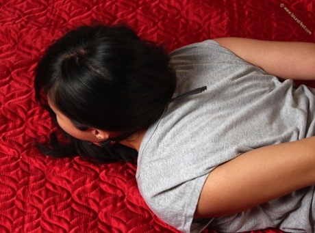 Face down: Dark-haired girl is left face down on a bed with her body resting in hog tie and gagged.