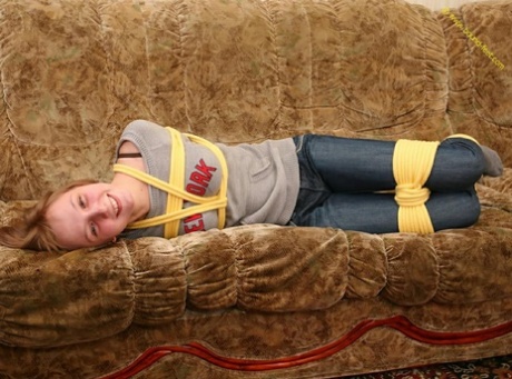 With her clothes tied tightly, a barefoot female struggles to balance on the couch.