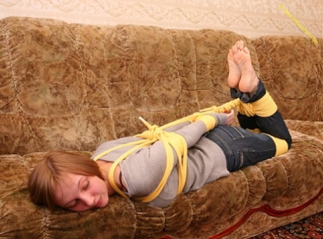 A woman who is barefoot struggles to stand on her couch while her clothes are tied loose.