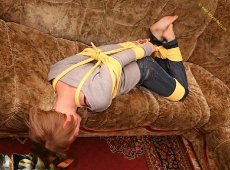 A woman who is barefoot struggles to stand on her couch while her clothes are tied loose.