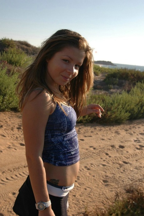 A charming girl exhibits her small tits and buttocks on a sandy beach.