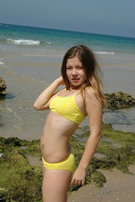 A charming 18-year old models herself in a yellow bikini on the beach.