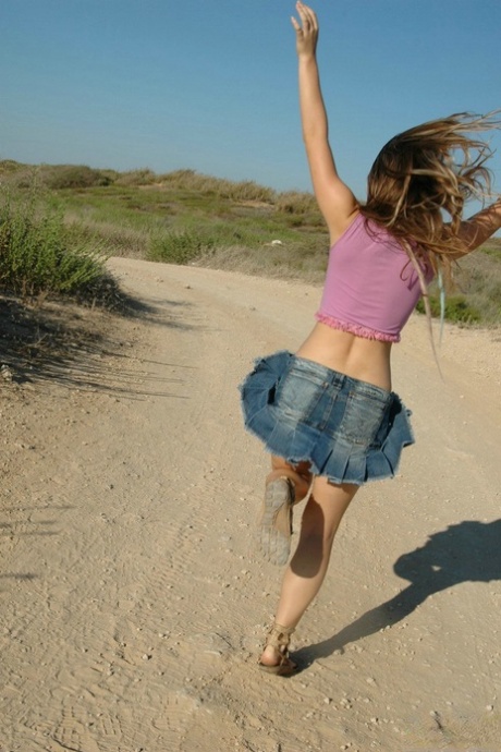 On a dirt road, an unidentified girl enjoys playing in the sun wearing a denim miniskirt and a thong.