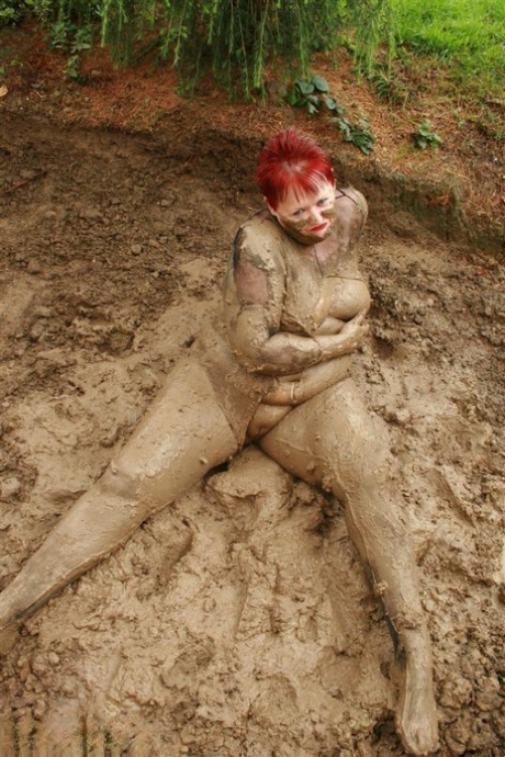 Vaginal exposed: The older redhead pooches in the middle of nothing while lying naked near her face in a mud pit.
