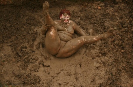 Older redhead Valgasmic Exposed rolls around in a mud pit while totally naked