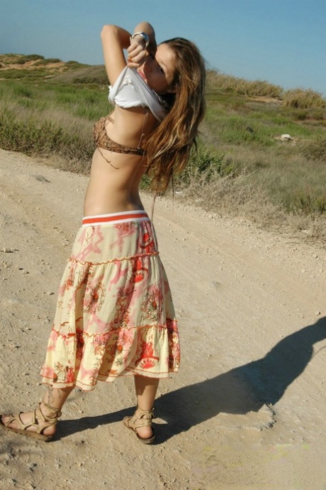 On a dirt road, an adorable young girl pins her pants while doing upskirt action.