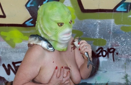 Naked British lady Speedy Bee eats a fish while wearing a costume mask