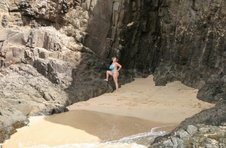 Curvy Claire, a slim British woman, exposes her breasts from her bikini in front of the ocean.