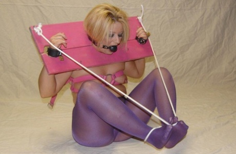 Wearing a pink stocking, a white woman performs a ball gag.