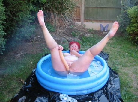 BBW Valgasmic Exposed, who is older and redheaded, engages in swimming activities while holding his dildo in a wading pool.