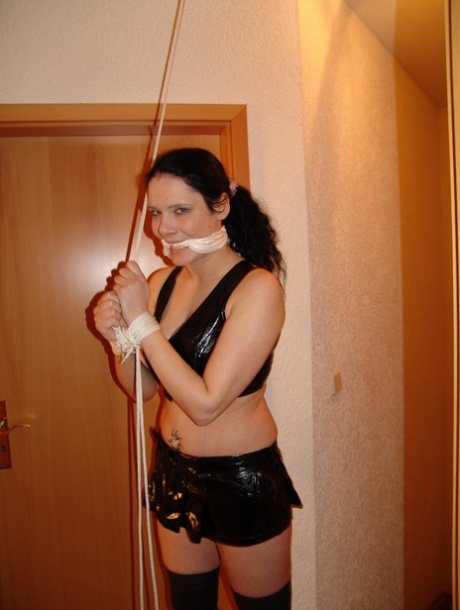 In a Brunette chic outfit, the woman is dressed in black latex and long boots while being tied up with ropes.