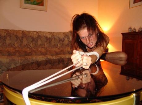 A coffee table is adorned with an exposed rope and a white girl sporting a cleave gag.