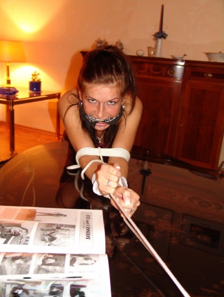 Rope tied over a coffee table: A white girl wears the ‘cleave gag’.