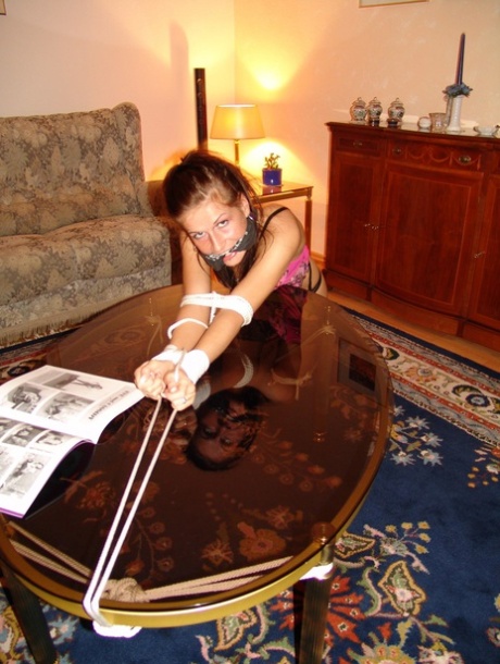 A coffee table is adorned with an exposed rope and a white girl sporting a cleave gag.