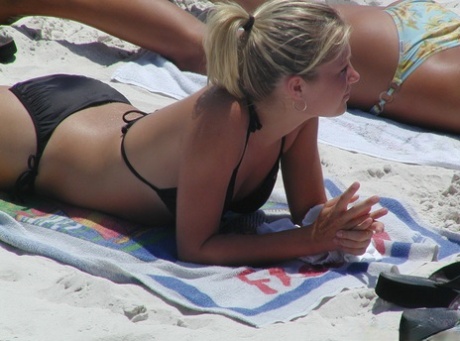 Women with tanned skinned bodies do swimsuits in tight fitting bikinis on the beach.