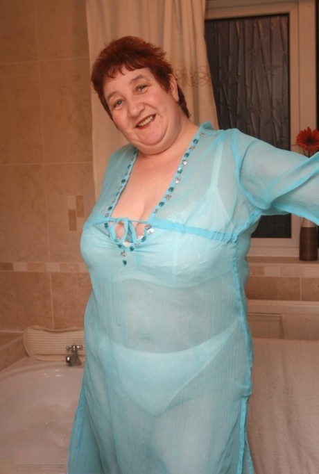 While fully clothed, Redhead nan Kinky Carol sits in a tub with her large figure.