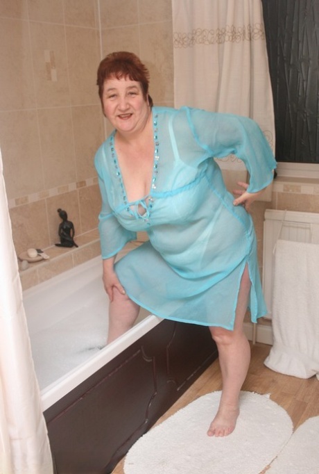 With her entire body fully clothed, Redhead nan Kinky Carol rests in a bathtub while she enjoys the experience.