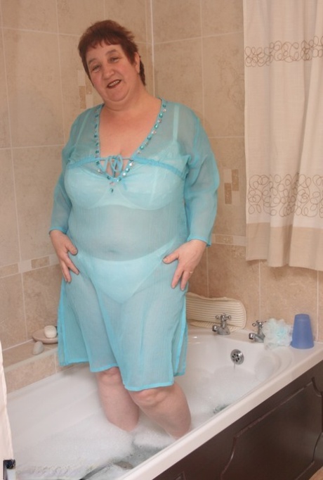 Redhead nan Kinky Carol is fully clothed and can be seen floating in a tub while sitting on the floor.