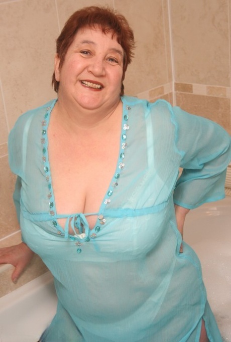 With her arms and legs fully covered, Redhead nan Kinky Carol enjoys herself atop her massive figure in a bathtub.