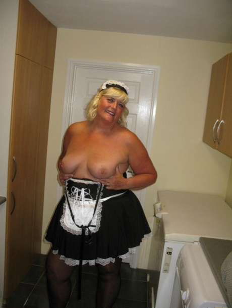 An overweight blonde maid named Chrissy Uk reveals herself in a kitchen while working.