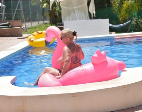 The older Melody, with blonde tattoos on her body swimsuit over an inflatable in a pool.