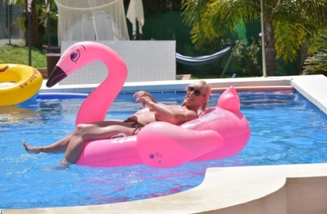 In a swimming pool, Melody with tattoos and an older age is seen floating on top of an inflatable.