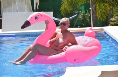 In a pool, Melody, an older woman with tattoos and blonde hair, goes without clothes on an inflatable boat.