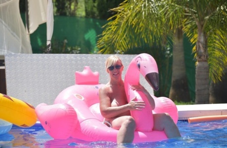 In a swimming pool, Melody, an older woman with tattoos, goes without clothing on an inflatable that she had to use.