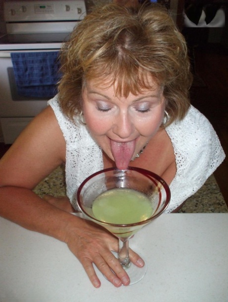 Busty Bliss, a grown-up woman with freckled breasts, flaunts her chest while drinking from an alcoholic beverage.