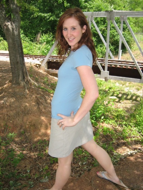 Near model railroad tracks, the pale redhead exposes her small breasts.