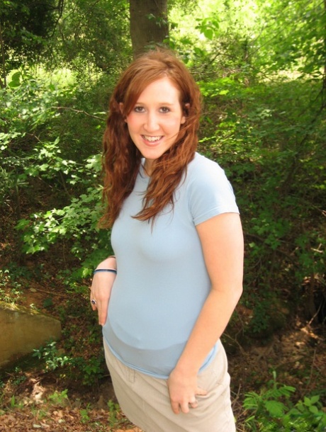 She reveals her pale red hair by exposing her small breasts near model railroad tracks.