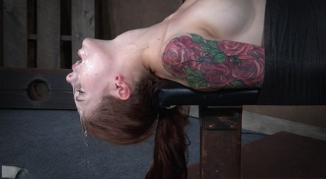 A bondage table is the site of a throat fucked by Anna De Ville, a tattooed woman.