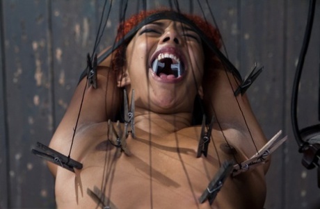 A black girl who is restrained screams out loud as she is tortured by a sadist.