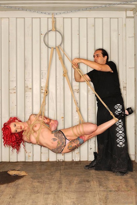 Becky Holt, a redhead fetish model with tattoos, was suspended by a rope during a performance in BDSM.