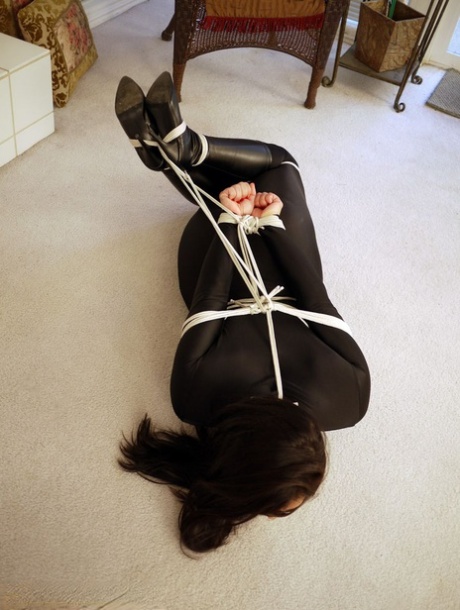 Clothed woman Tomiko is tied up with rope while tape is applied over her mouth to silence it.