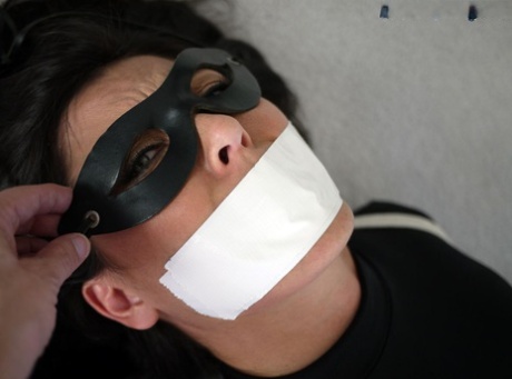 While tied up with rope, Tomiko the woman in revealing clothing is silenced with tape over her mouth.