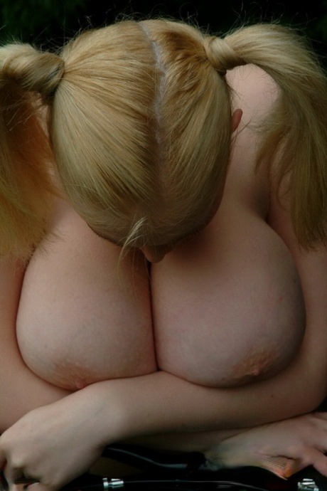 BBW Ashley Sage Ellison, who is blonde and has been biking, shows off her massive pigtails with her hands on her legs.