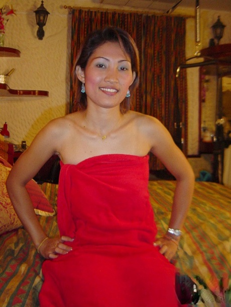 The thin Thai girl exposes her natural tits while removing her red dress on the bed.