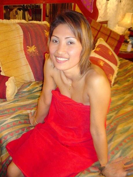 A thin Thai girl removes her red dress on the bed and displays all of her natural tits.