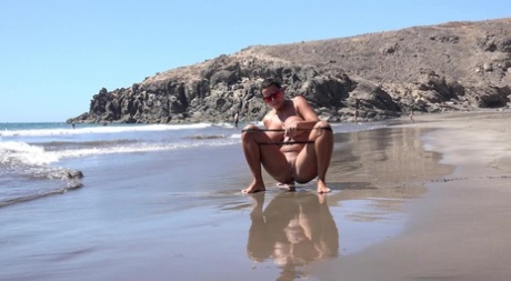 Chloe Lamour, a woman with big breasts, pees while lying on the beach.