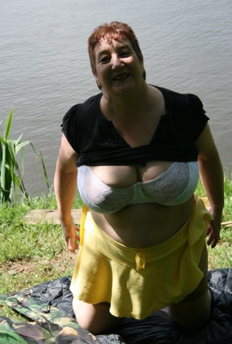 An older redhead named Kinky Carol puts on a bra and layers of clothing near the water.