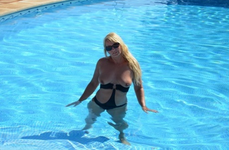 Sweet Susi, a blonde woman in her middle age, releases her breast tissue from a pool towel.